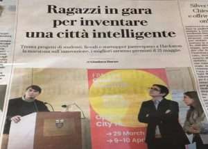 Ritaglio di giornale con articolo su un hackathon per la città intelligente, con titolo grande, testo e foto dei partecipanti.