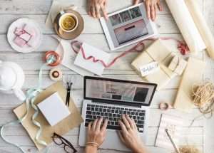 Immagine decorativa di una scrivania con laptop, tablet e materiali per confezioni regalo.