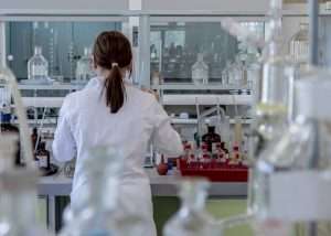 Foto di laboratorio scientifico con ricercatrice di spalle al banco di lavoro.