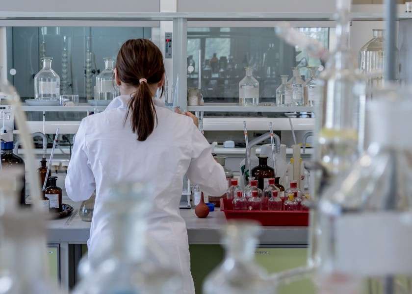 Foto di laboratorio scientifico con ricercatrice di spalle al banco di lavoro.
