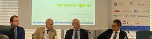 Quattro persone sedute a un tavolo durante un convegno. Schermo con titolo “Transizione Digitale” sullo sfondo.
